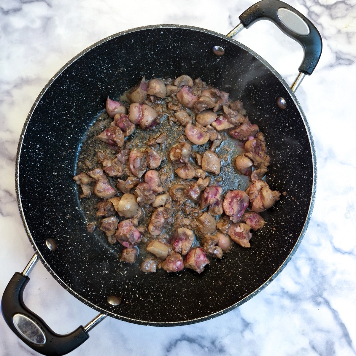 Pieces of kidney browning in a frying pan.