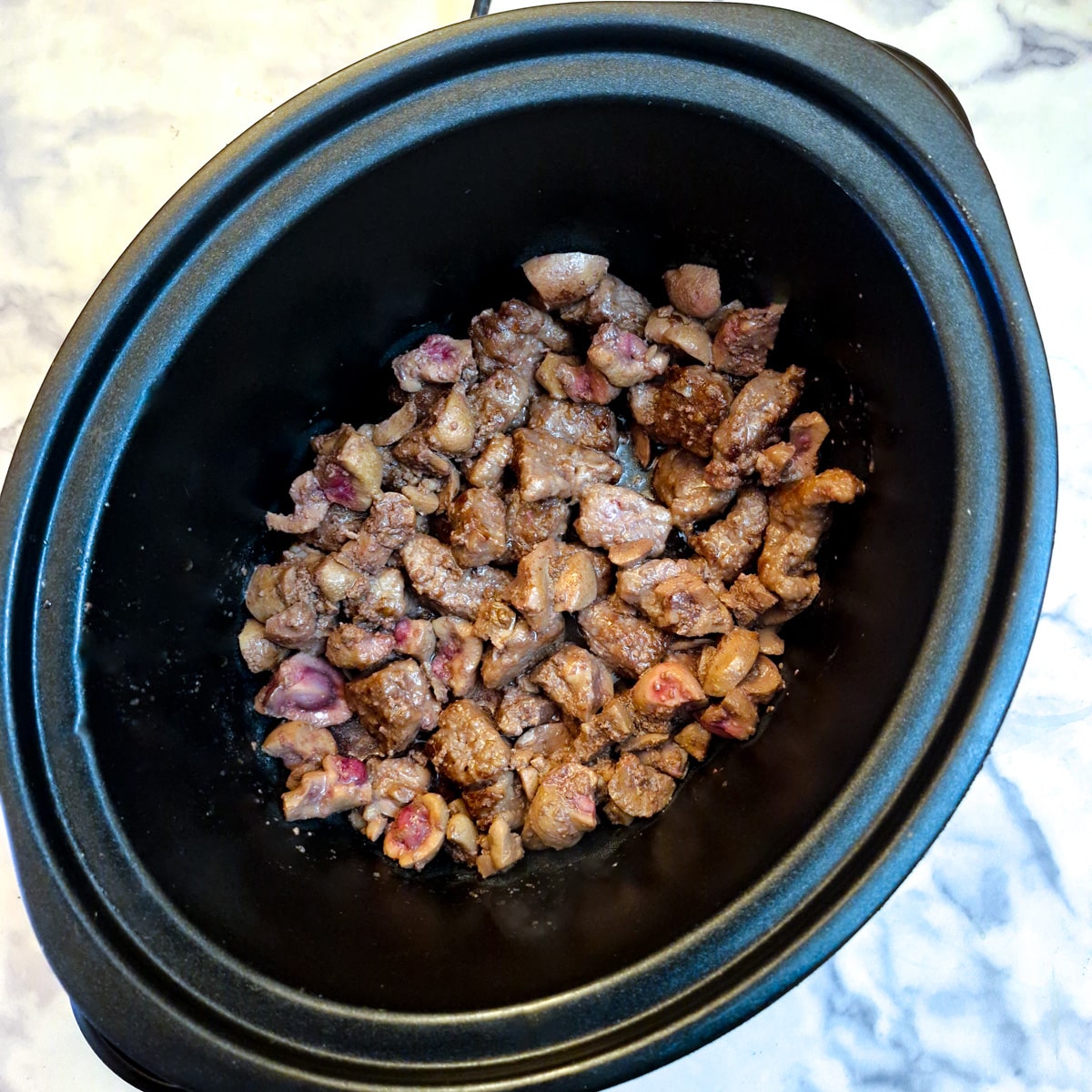 Pieces of steak and kidney in the inner pot of a slow-cooker.