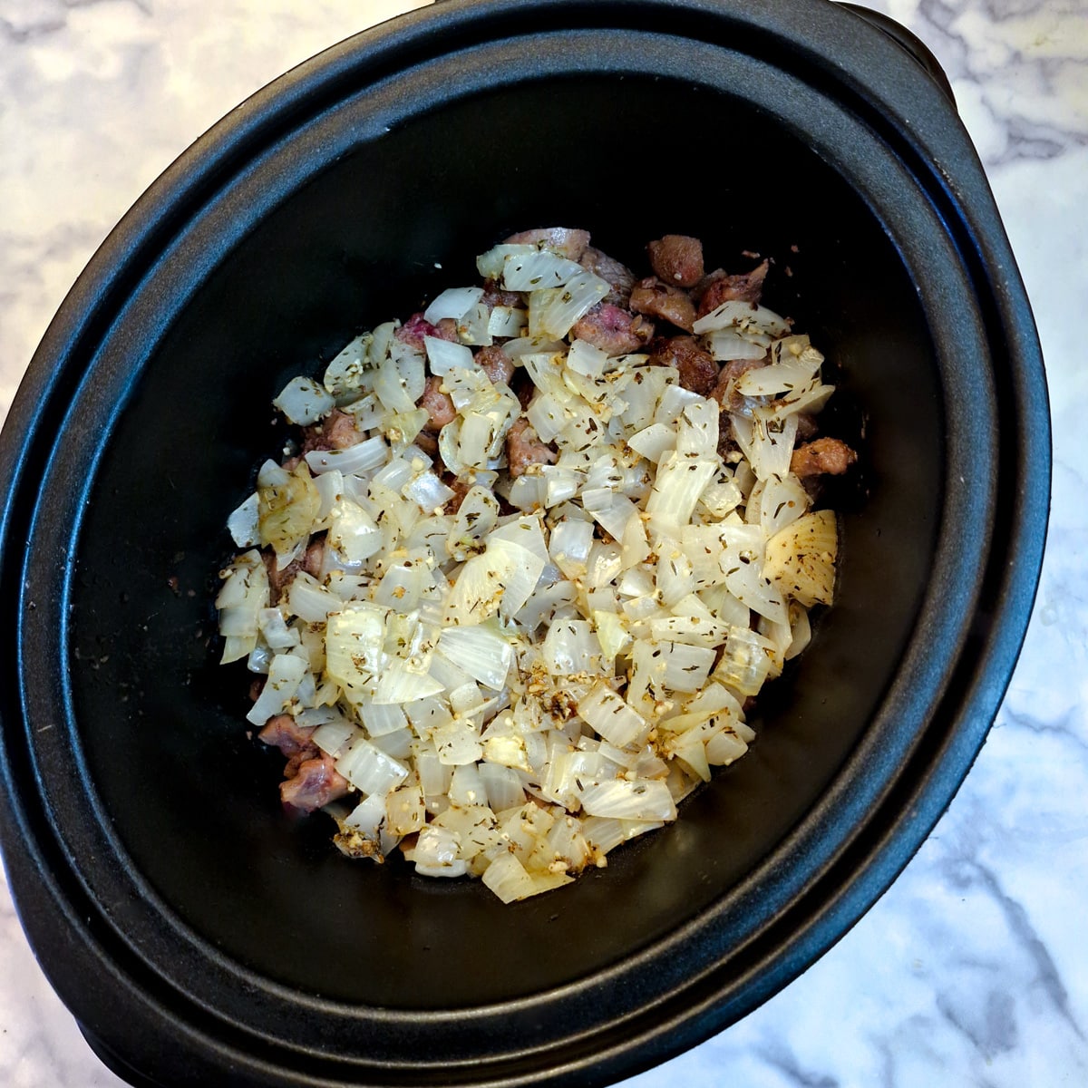 Chopped onions added to meat in a slow-cooker.