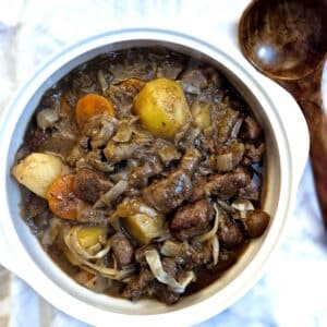 Overhead shot of a white serving bowl filled with beef and kidney stew. There is a large wooden spoon at the side of the bowl.