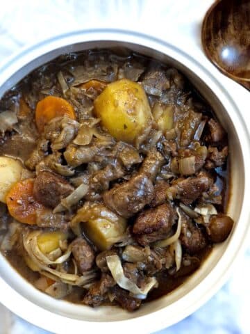 Overhead shot of a white serving bowl filled with beef and kidney stew. There is a large wooden spoon at the side of the bowl.