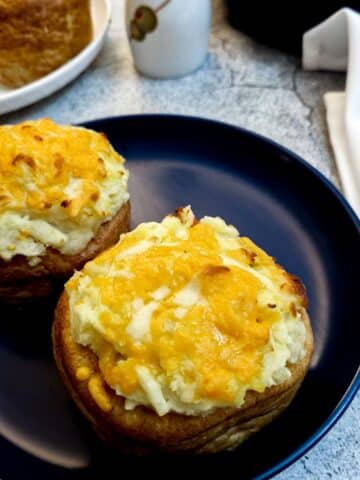 Two stuffed Yorkshire pudding pies on a blue plate, in front of a dish of green salad.