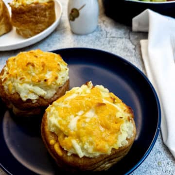 Two stuffed Yorkshire pudding pies on a blue plate, in front of a dish of green salad.