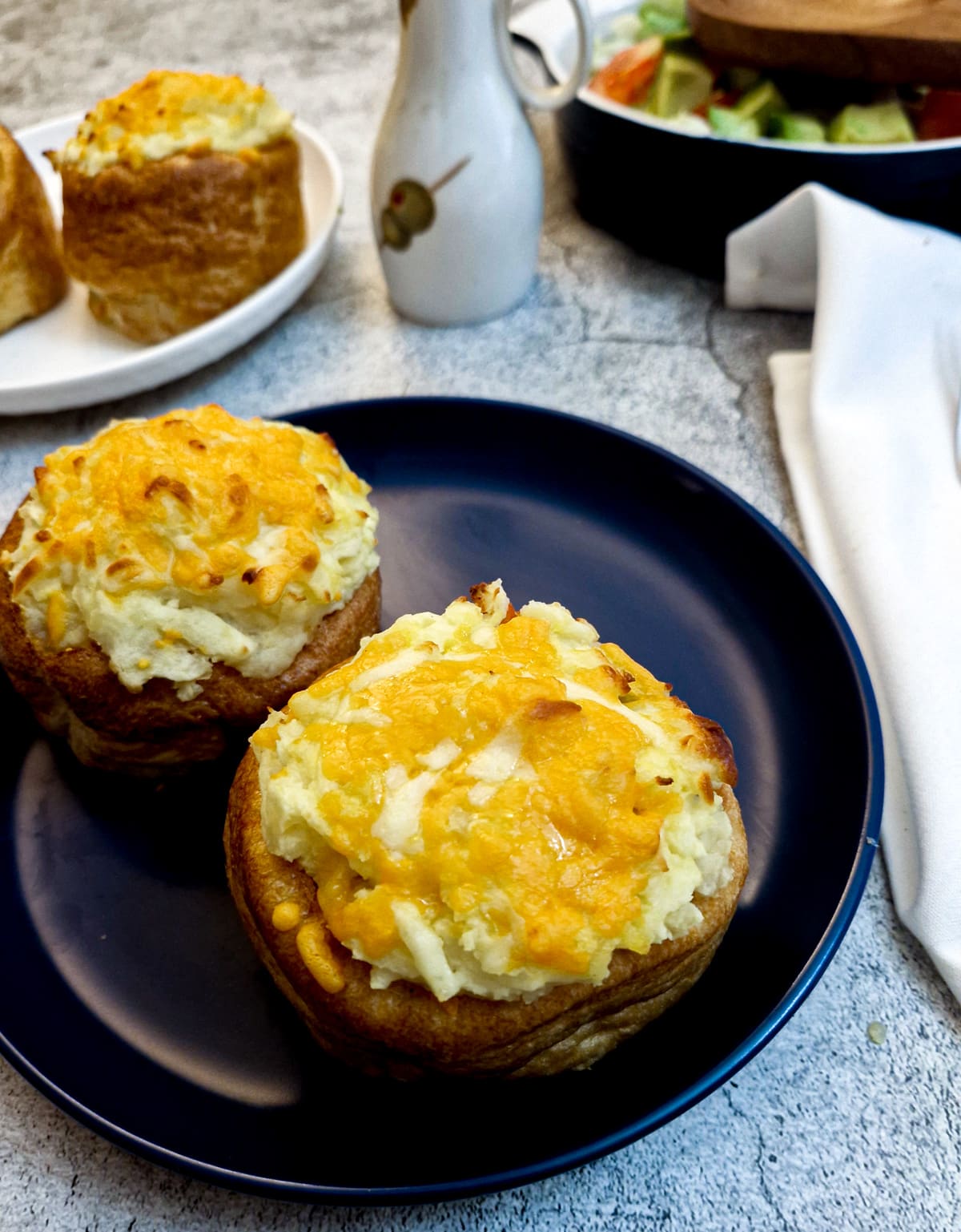 Two stuffed Yorkshire pudding pies on a blue plate, in front of a dish of green salad.