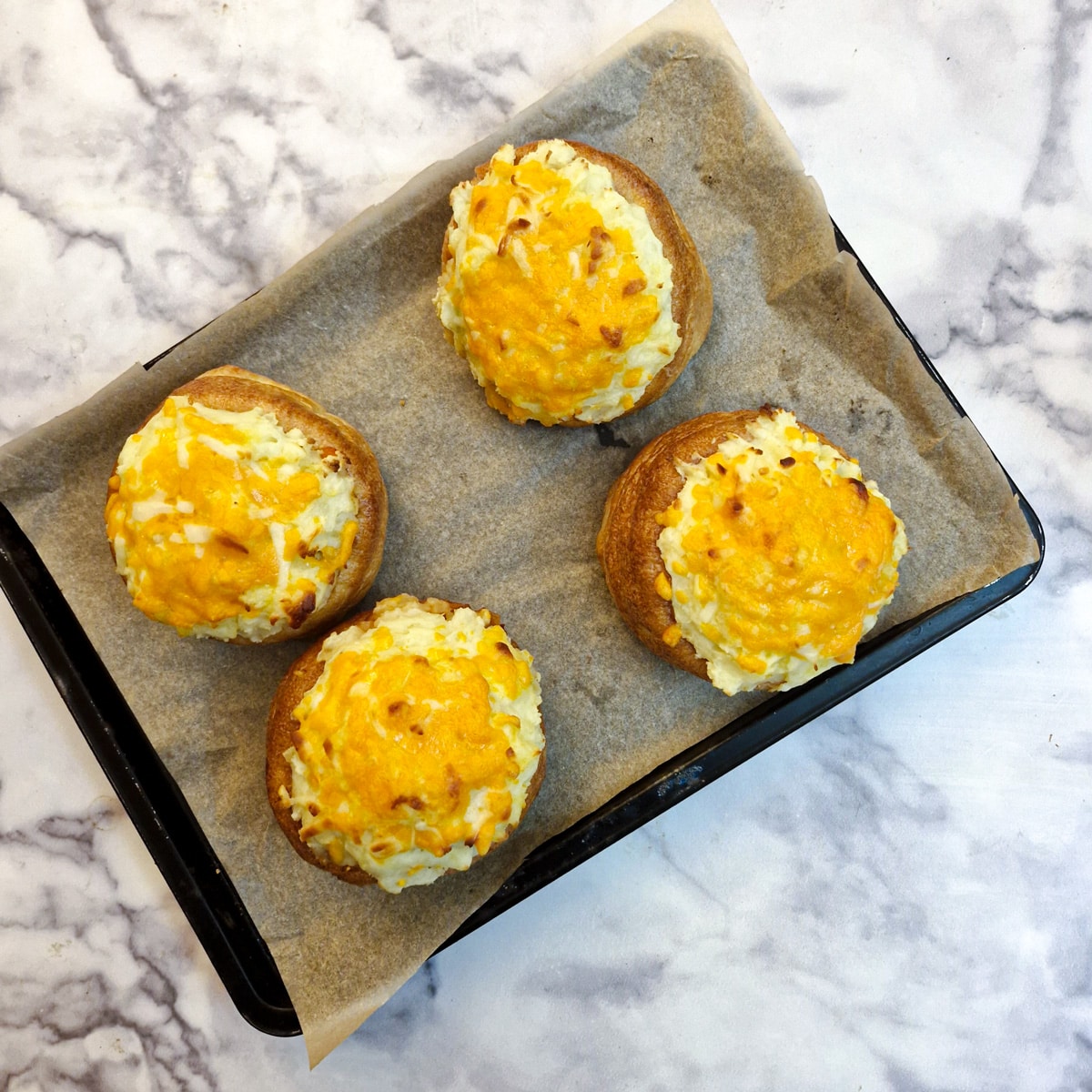 4 browned stuffed Yorkshire pudding pies on a baking tray.