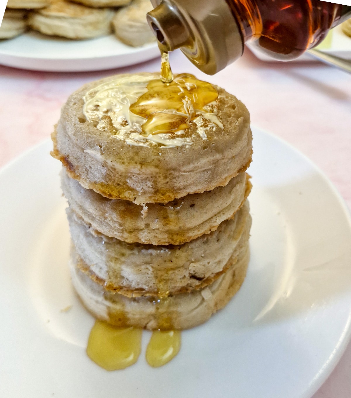 4 crumpets in a pile, with syrup being drizzled over them.