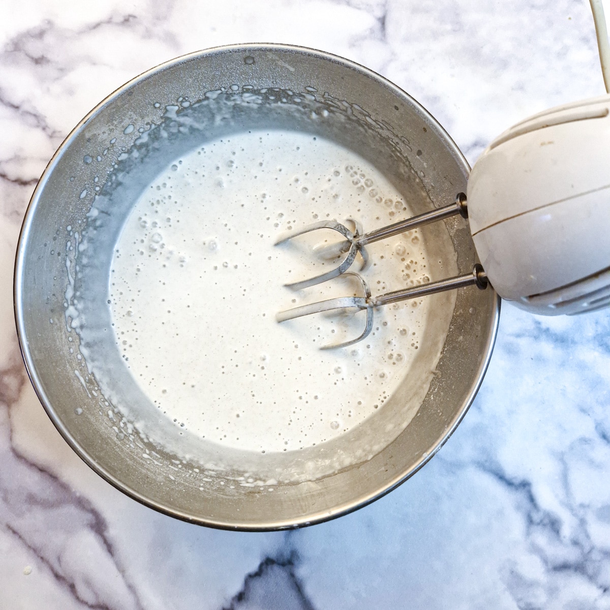 Flour and water being mixed in a round metal bowl with a hand blender.