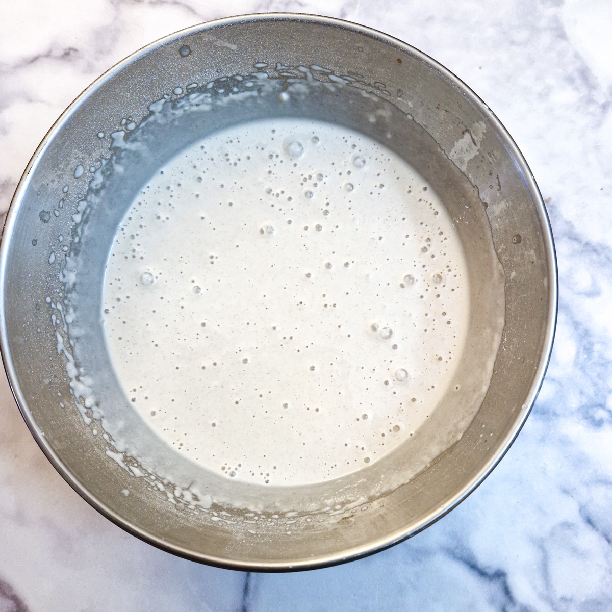 A round metal bowl with mixed crumpet batter.