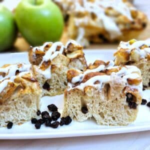 4 slices of apple and raisin focaccia on a white plate with apples in the background.