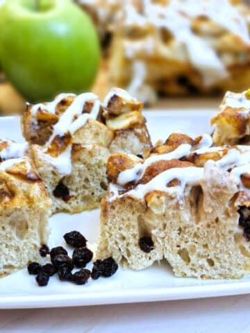 4 slices of apple and raisin focaccia on a white plate with apples in the background.