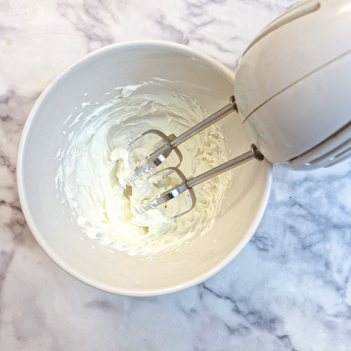 Cream cheese being blended with an electic hand beater.