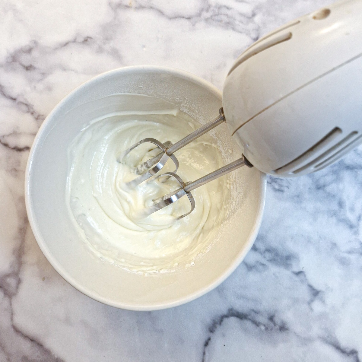 Cream cheese and icing sugar being blended with an electric hand beater.