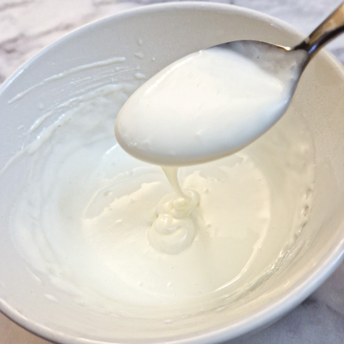 Cream cheese frosting being dripped from a spoon held above a small white bowl.