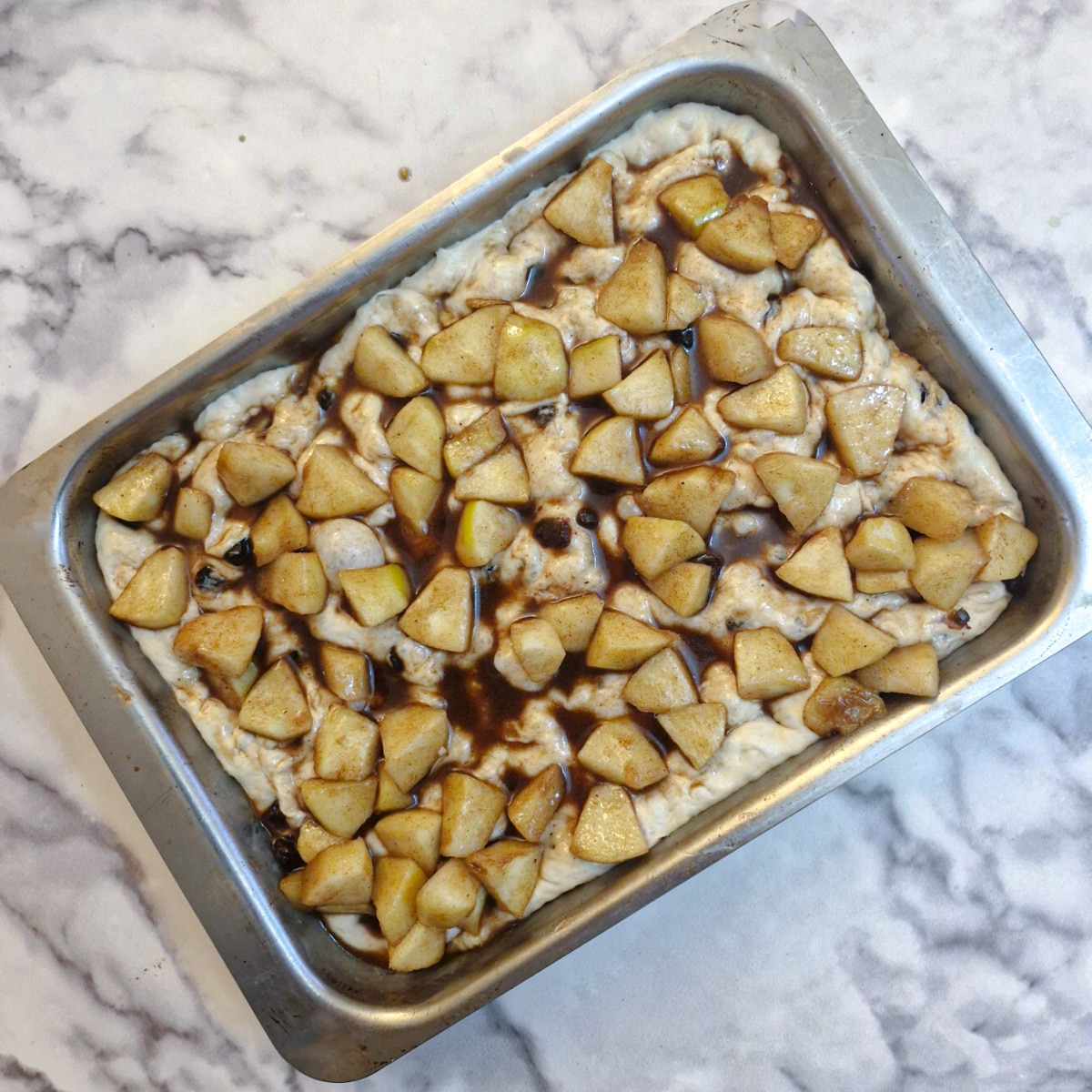 Pieces of softened apple arranged on focaccia dough in a baking dish.