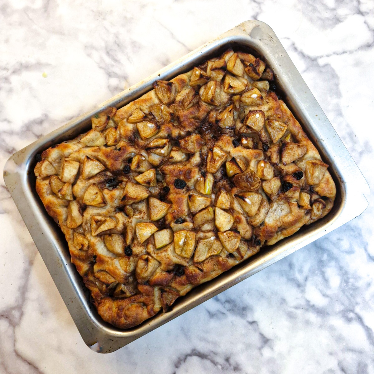 A baked apple and raisin focaccia in a baking dish.