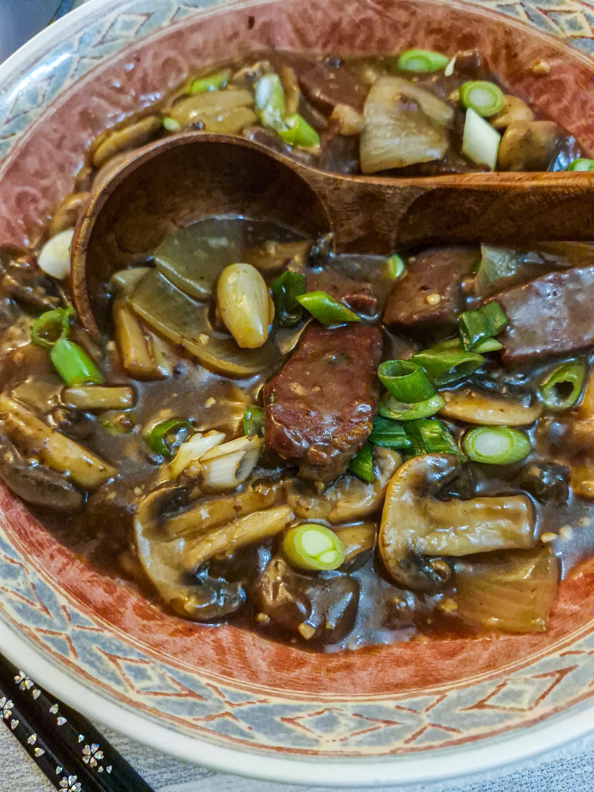 Closeup of beef and mushroom stirfry in a serving dish with a wooden spoon.