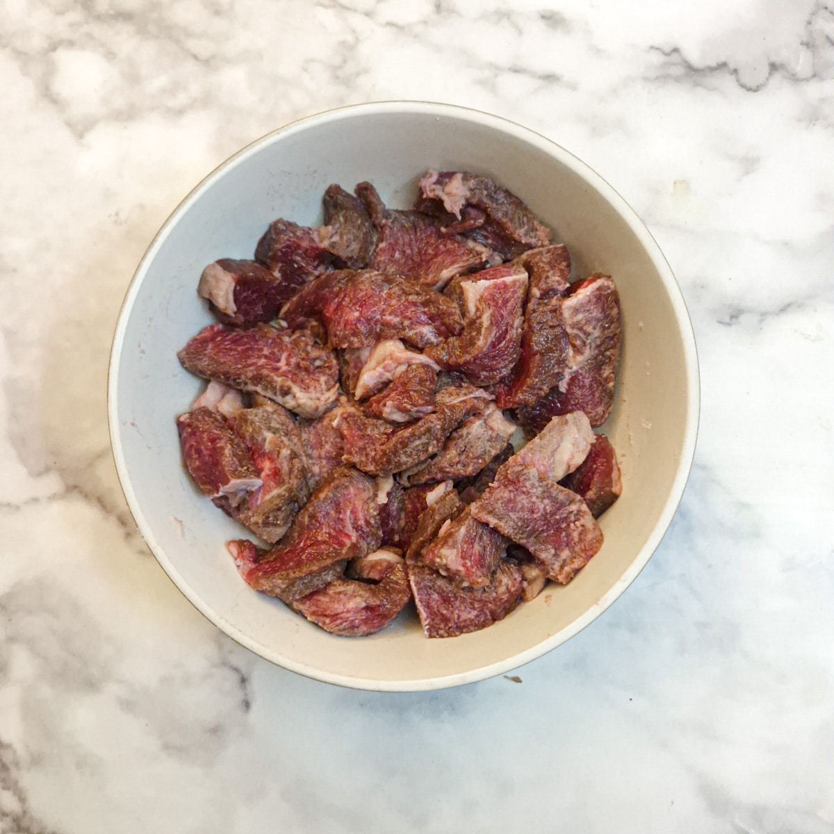 Pieces of steak in a white bowl.