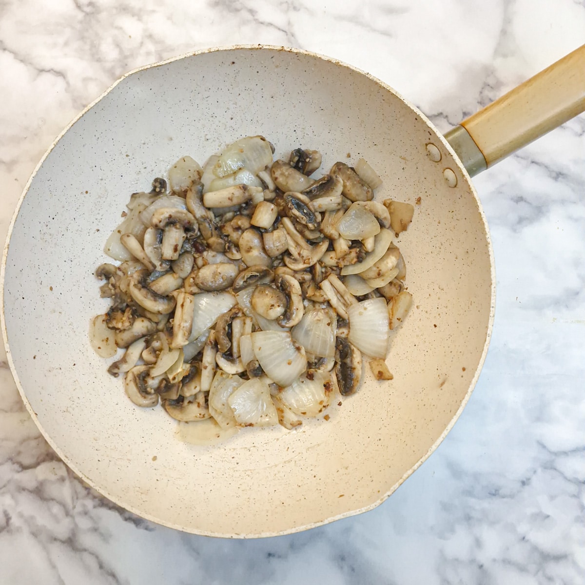 Mushrooms and onions frying in a wok.