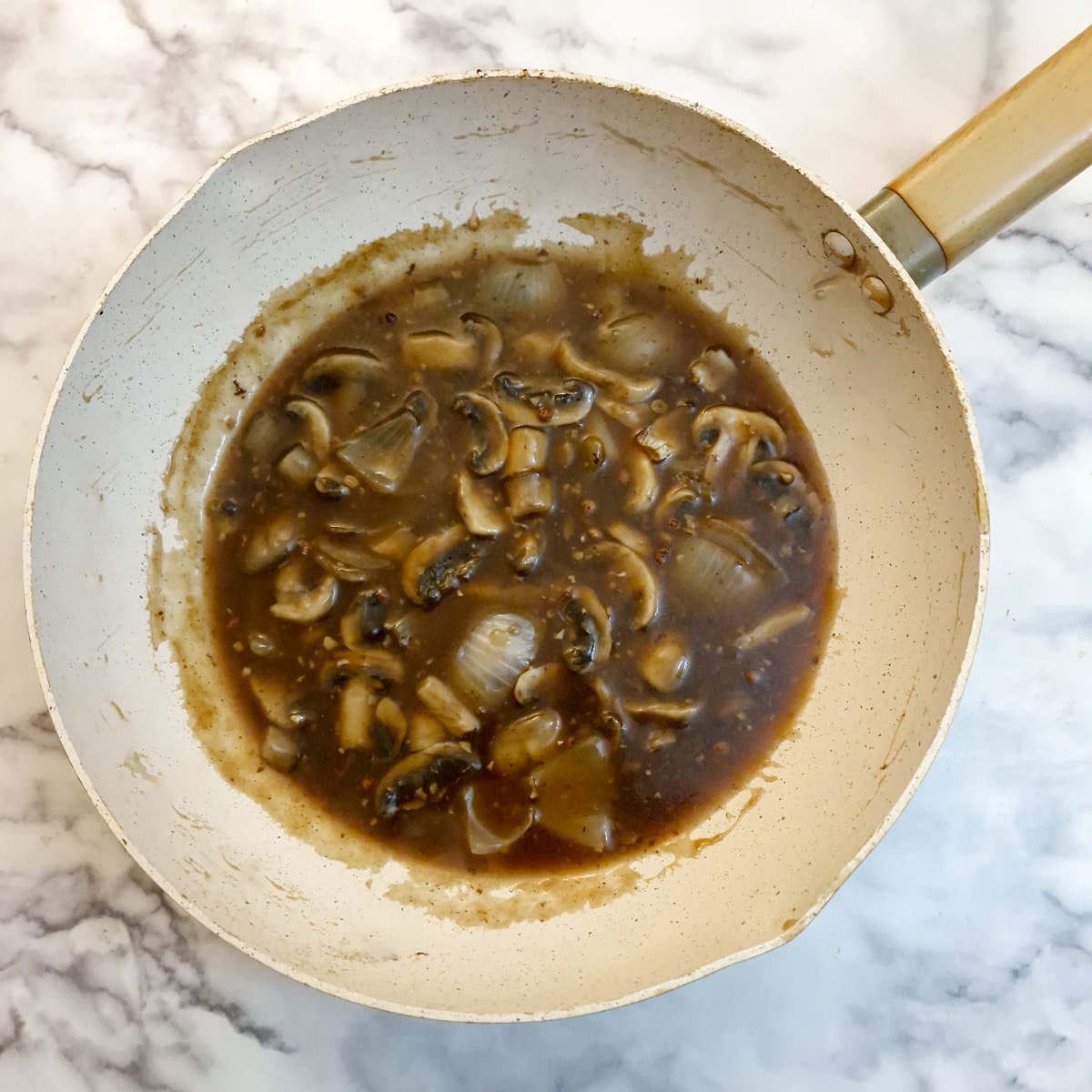 Thickened sauce with onions and mushrooms in a wok.