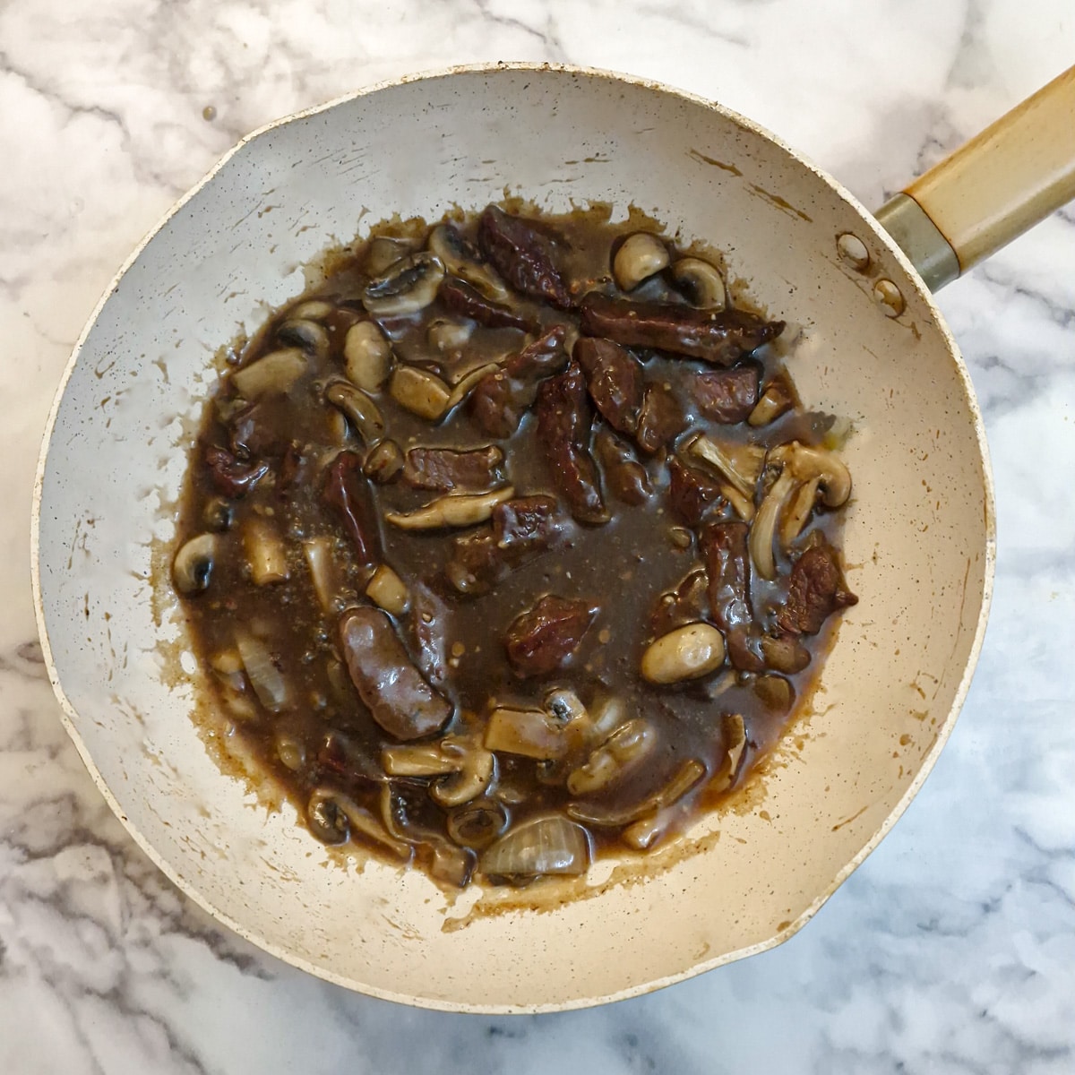 Fried beef strips added to mushroom sauce in a wok.