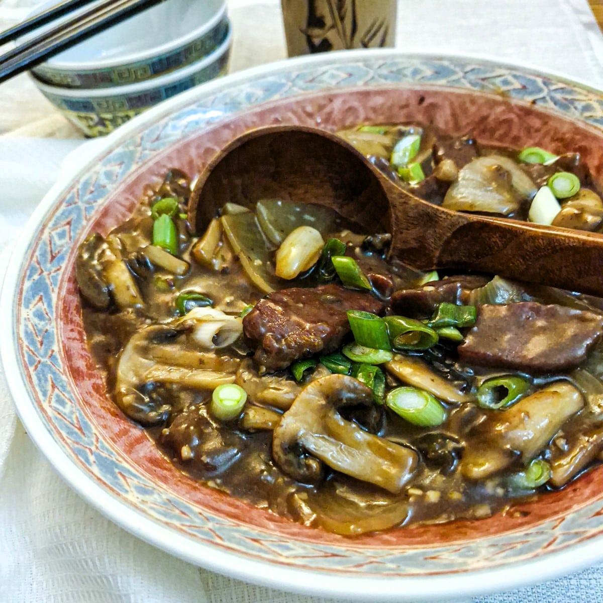 Beef and mushroom stirfry in a pink and blue patterned serving dish.