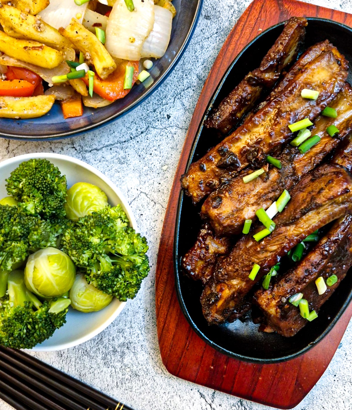 Overhead shot of a dish of pork spareribs with salt and pepper chips and steamed green vegetables on the side.