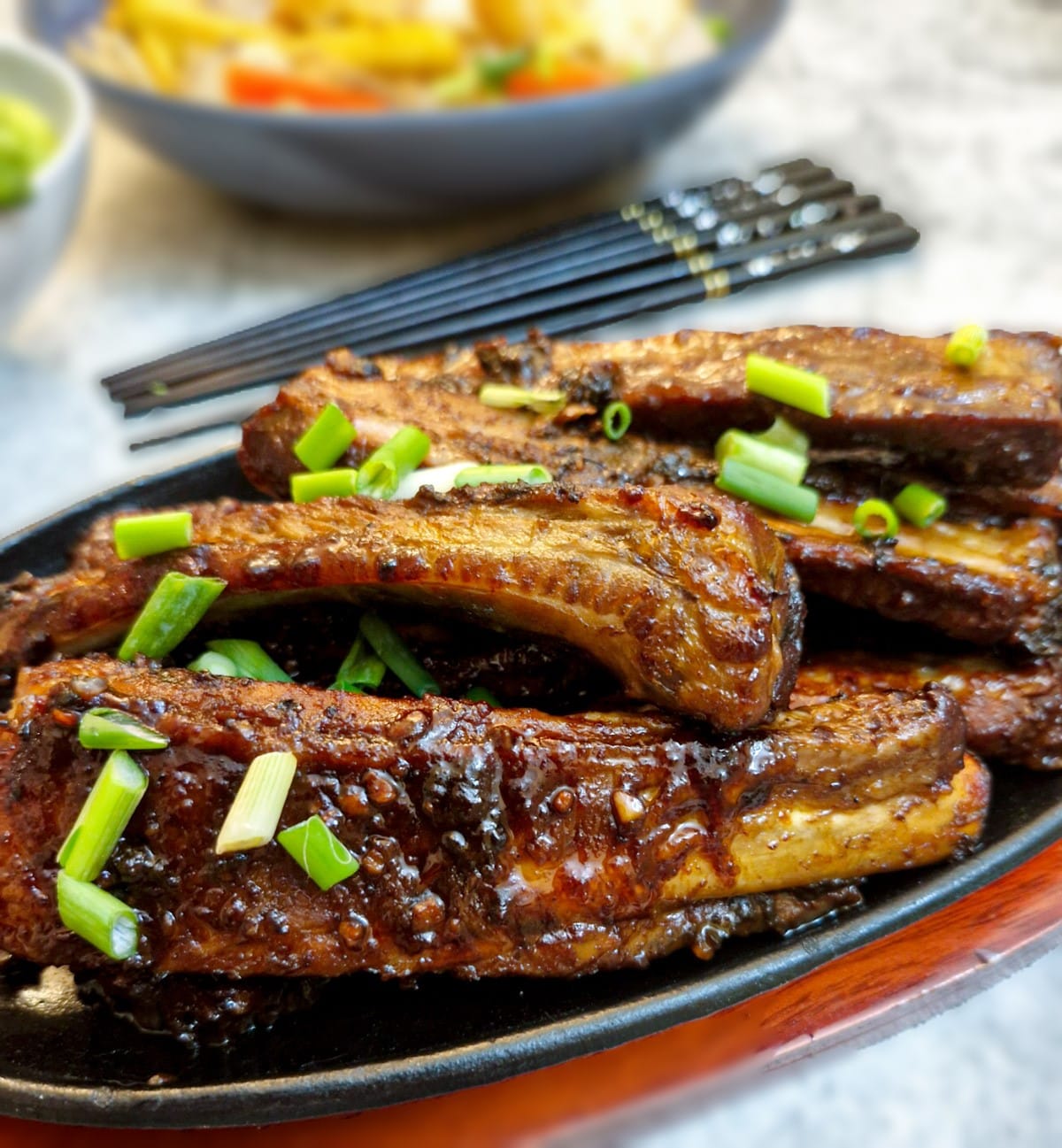 Close up of pork spareribs on a plate with chopsticks in the background.