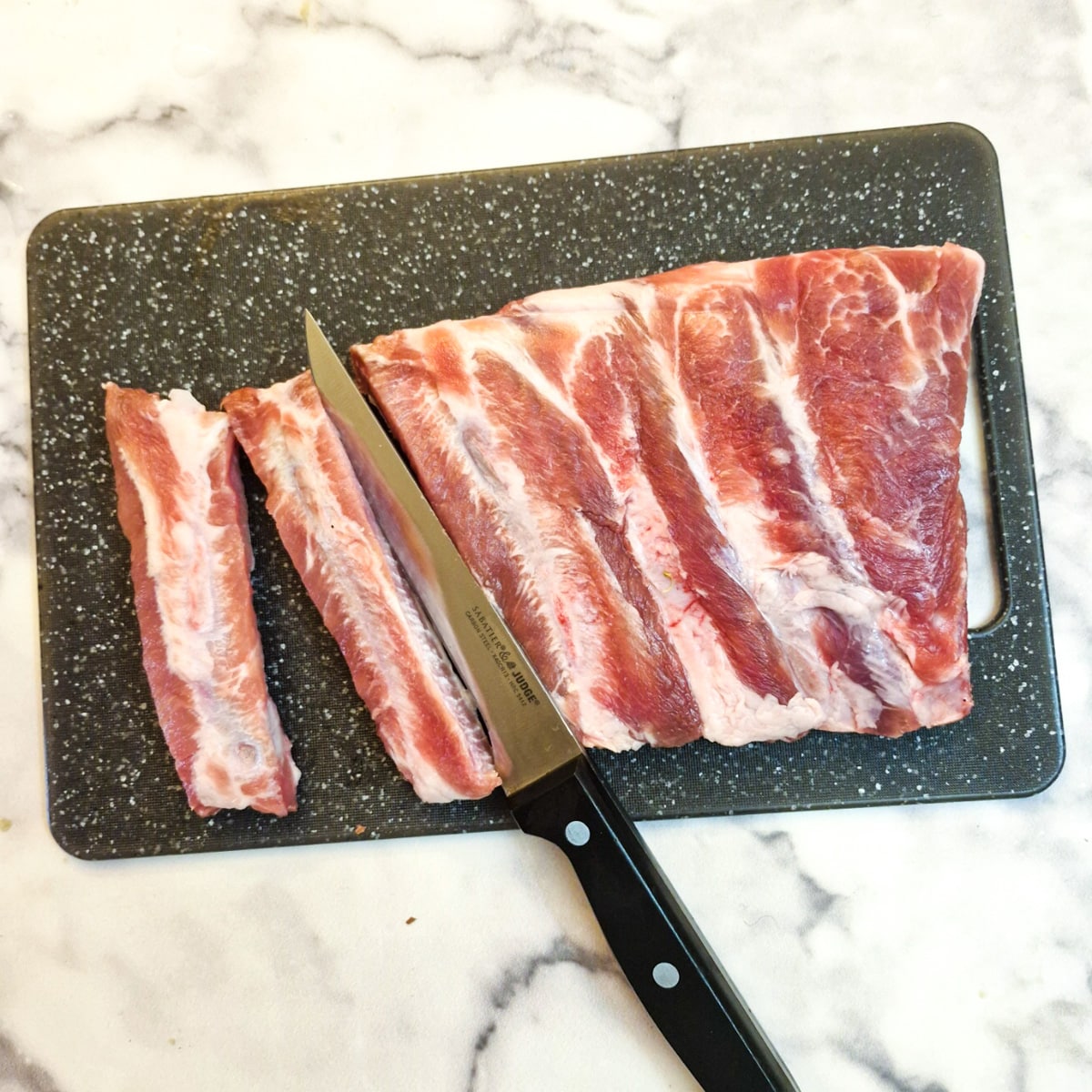 A rack of pork spare ribs being separated into individual ribs with a sharp knife.