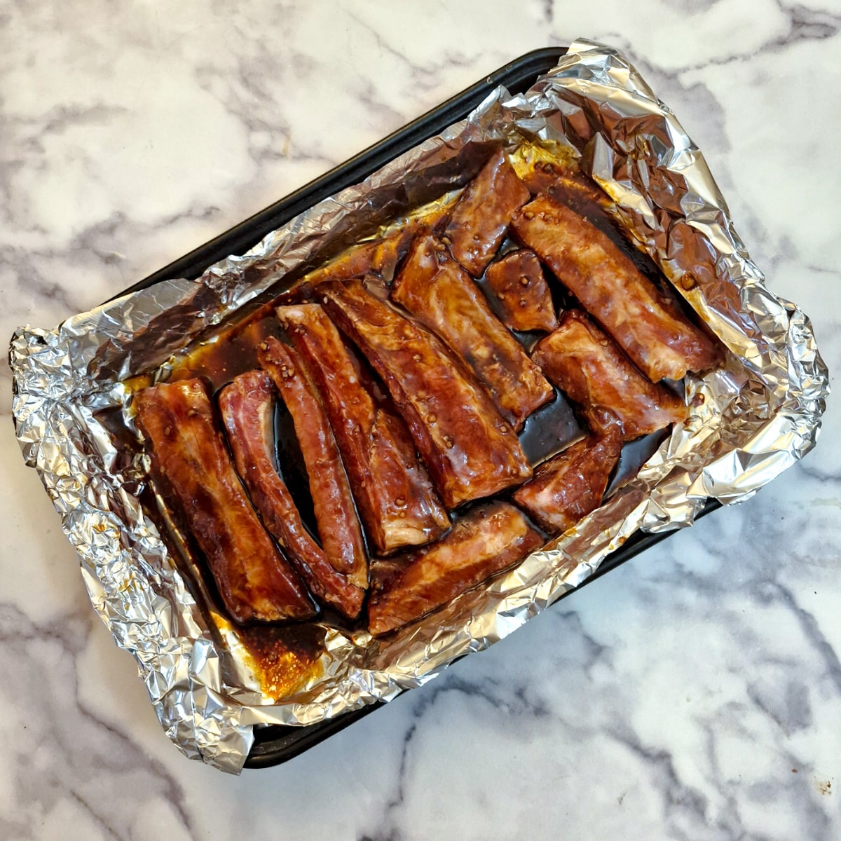 Pork ribs coated with marinade in a foil-lined baking dish.