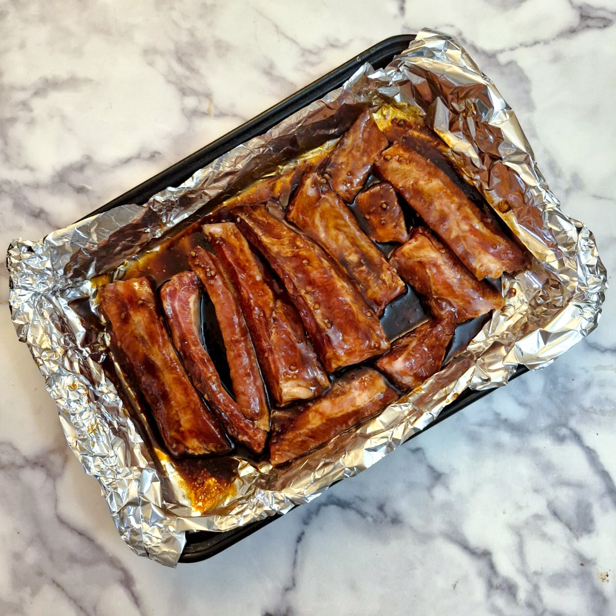 Pork ribs coated with marinade in a foil-lined baking dish.