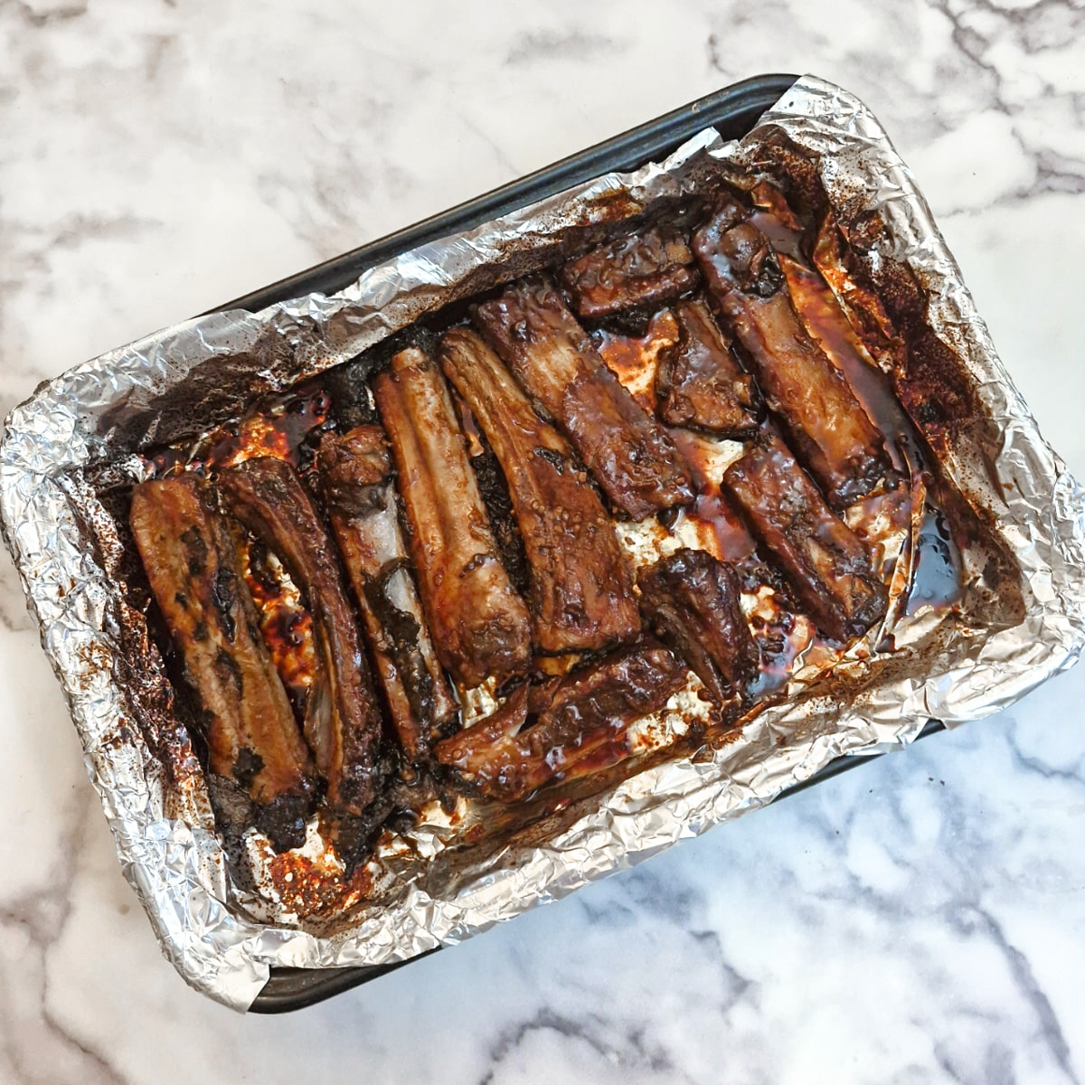 Baked pork spareribs in a foil-lined baking dish.