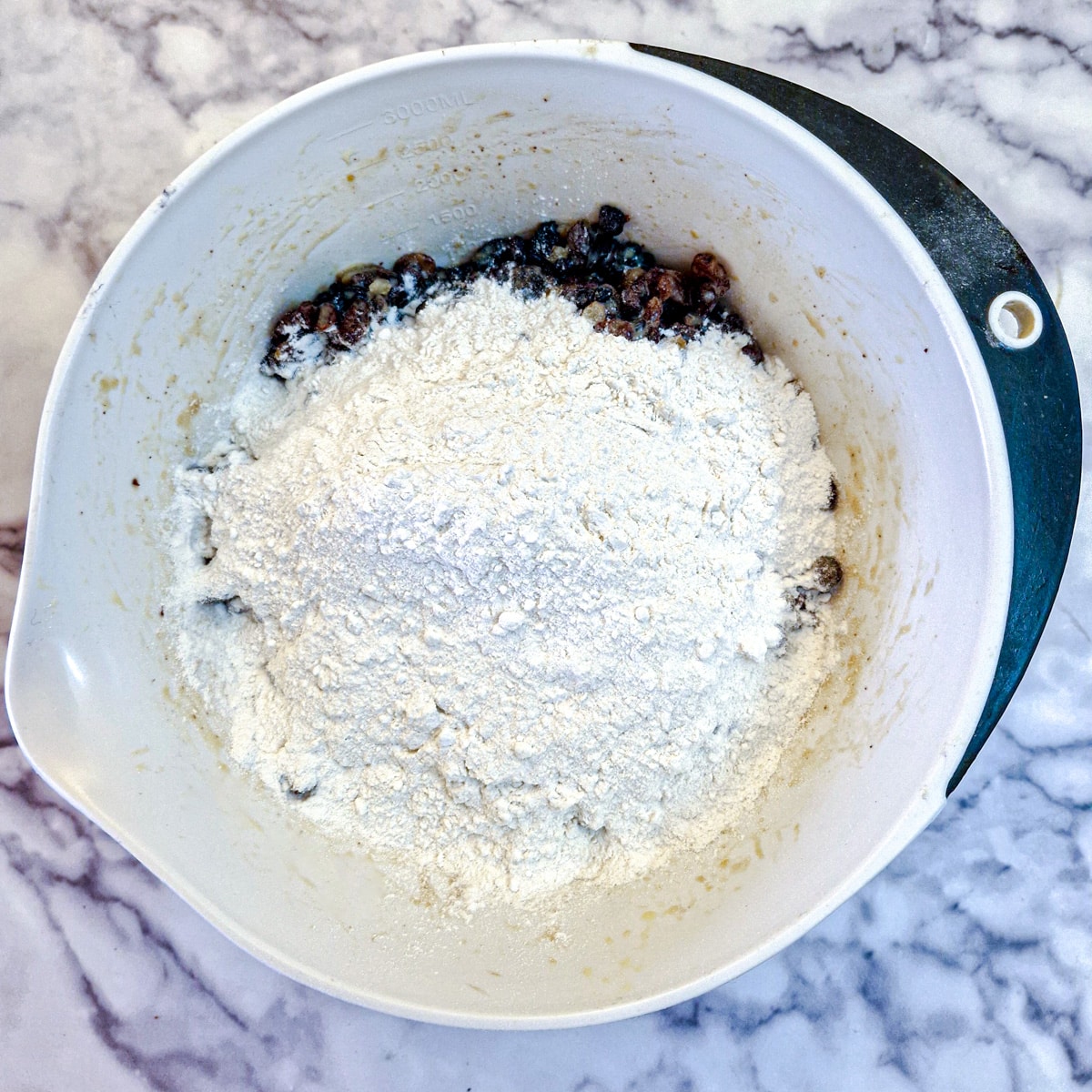 Flour added to the soaked mixed fruit in a mixing bowl.