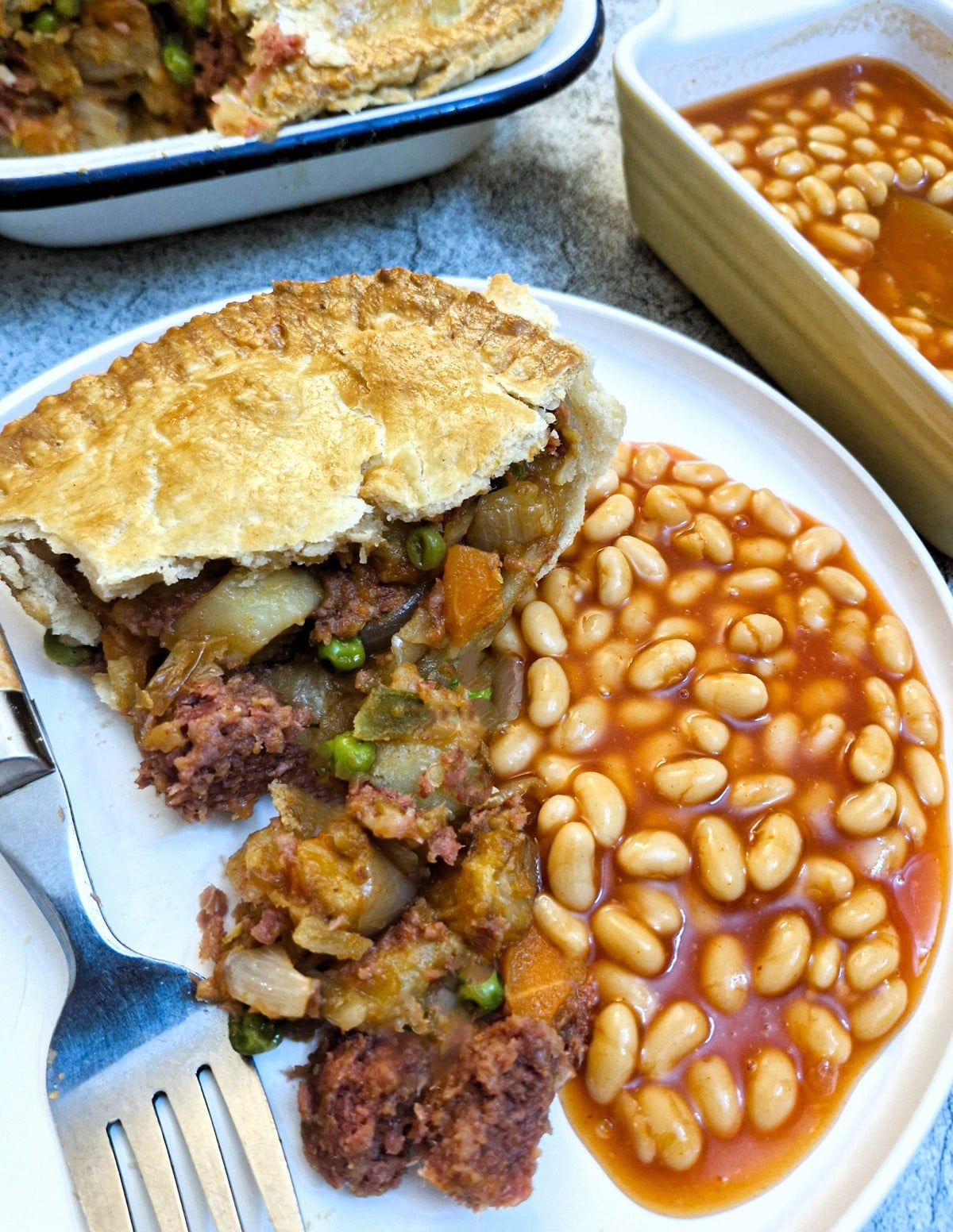 A slice of corned beef and potato pie on a white plate, with a helping of baked beans.