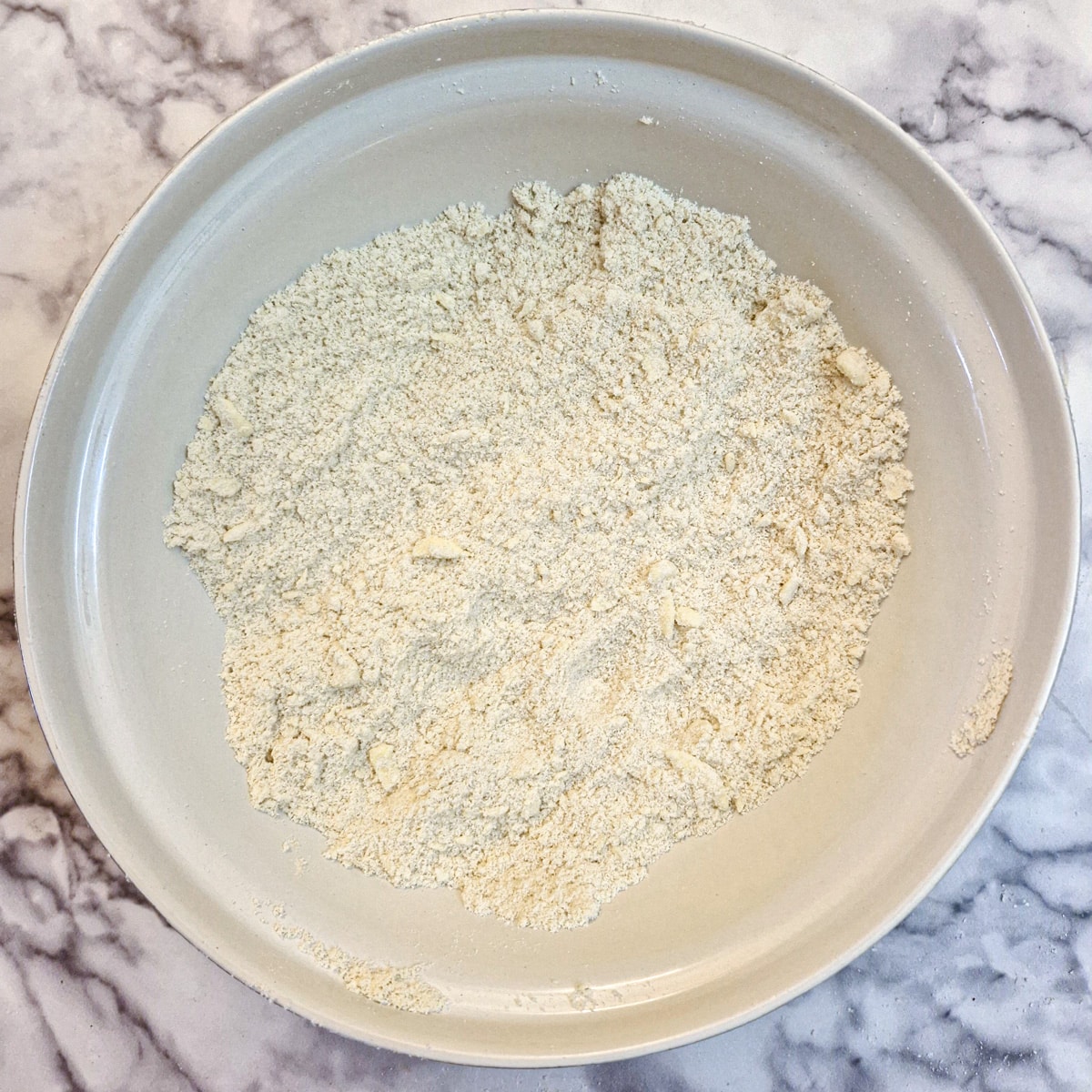 Flour and butter rubbed together to form breadcrumbs in a large white mixing bowl.