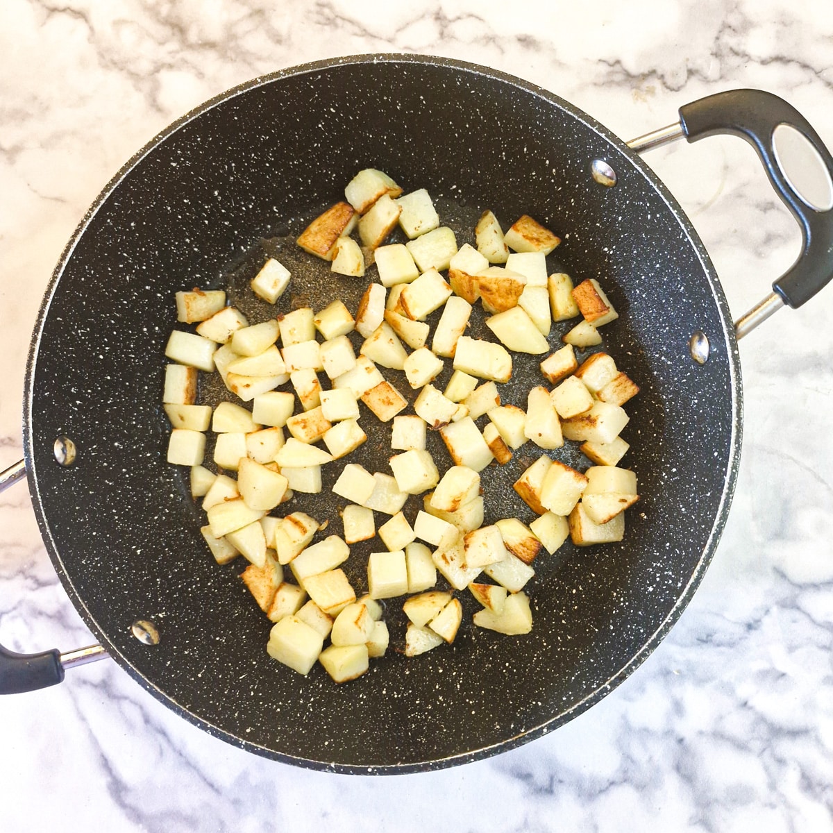 Cubed potatoes browning in a saute pan.