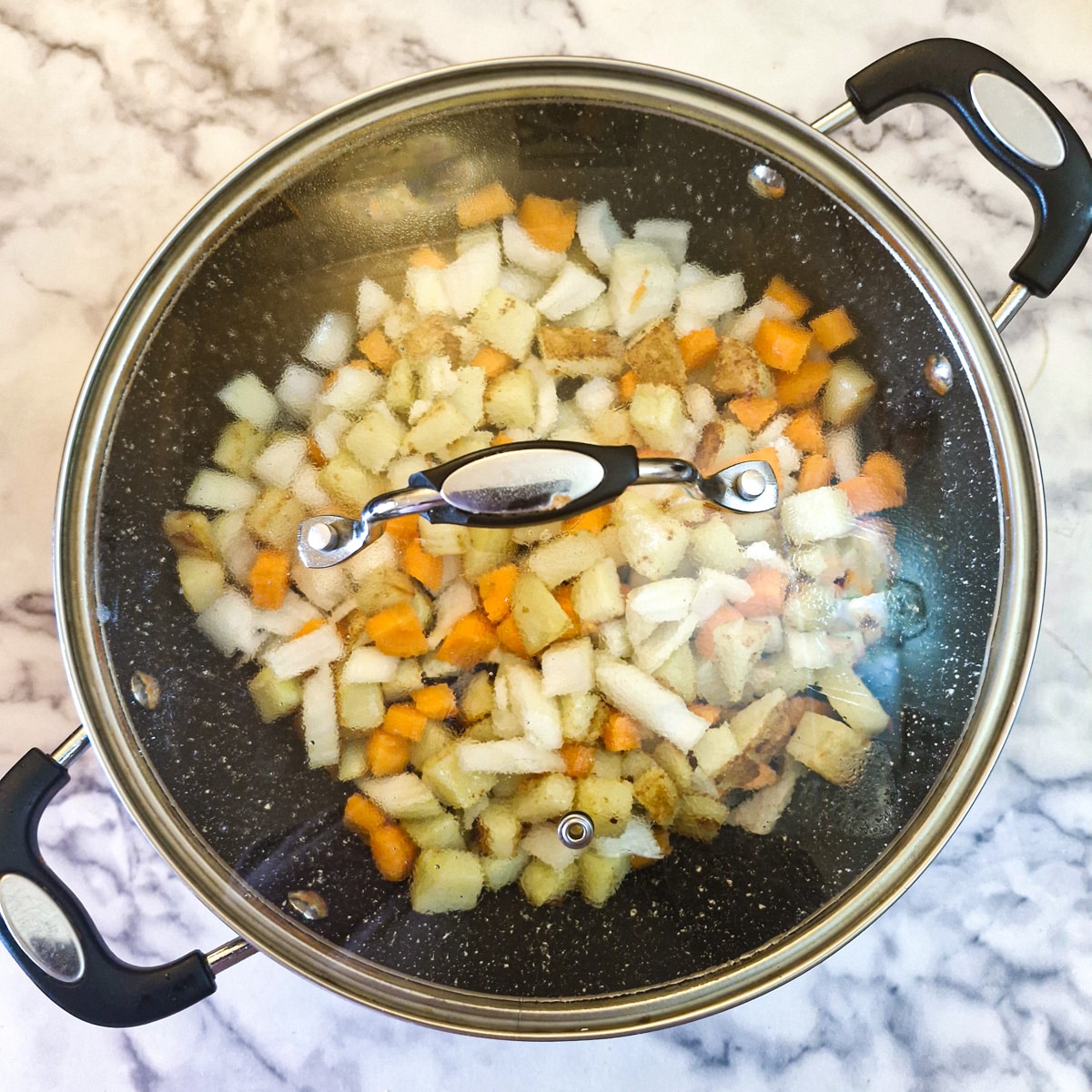 Carrots, potatoes and onions in a saute pan covered with a glass lid.