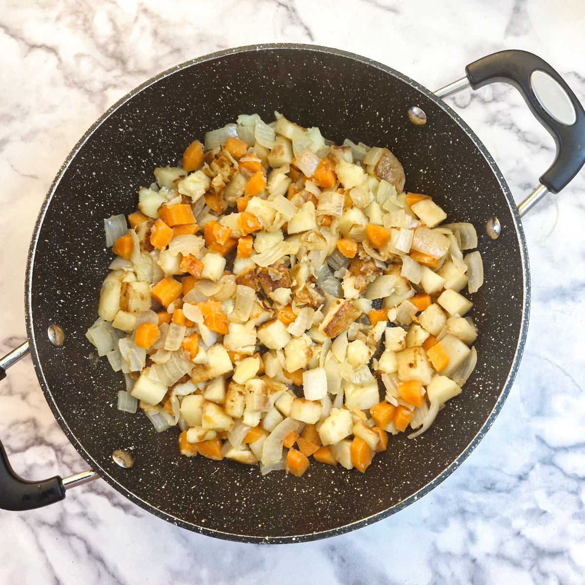 Soiftened potatoes, carrots and onions in a saute pan.