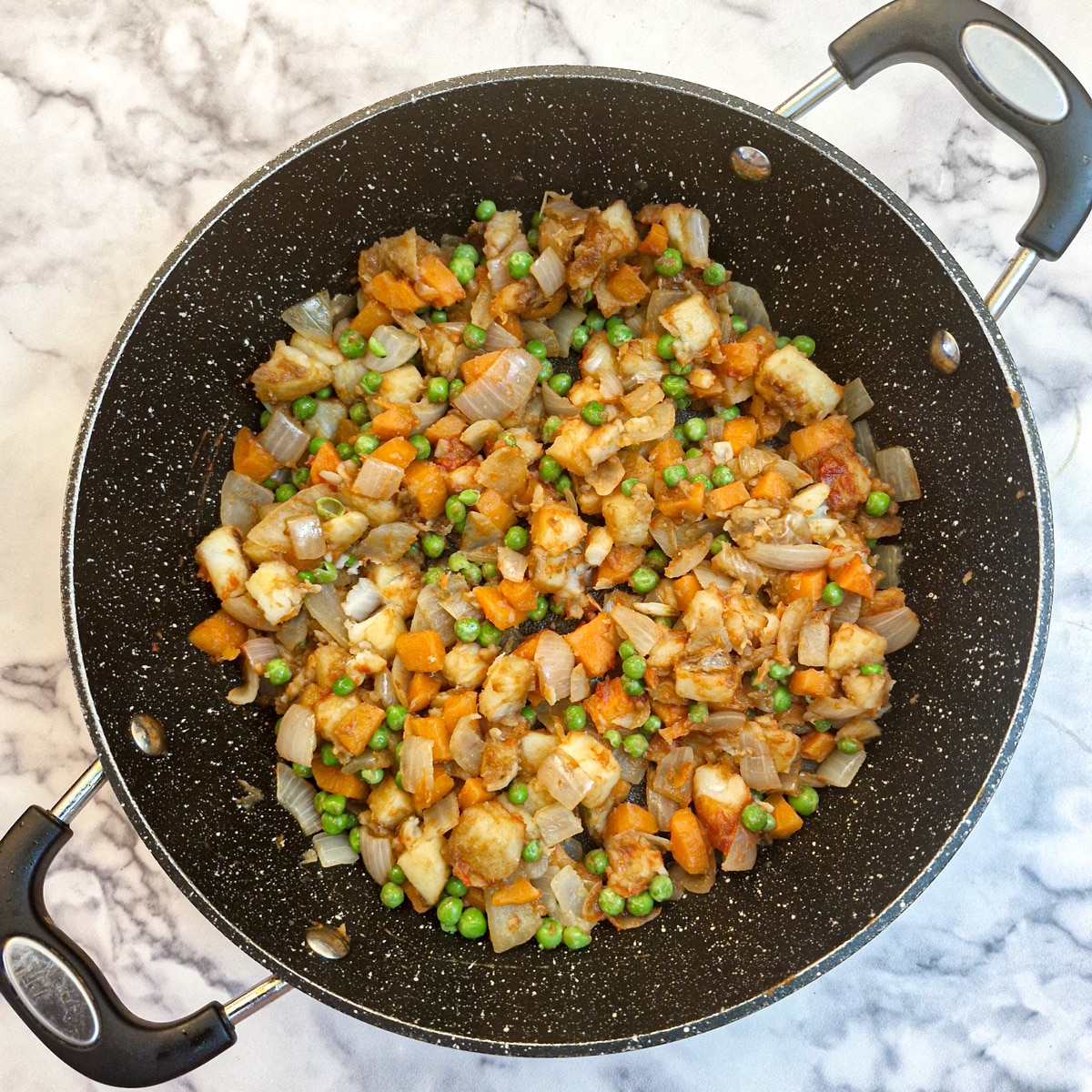 Peas mixed with potatoes, carrots and onions in a saute pan.