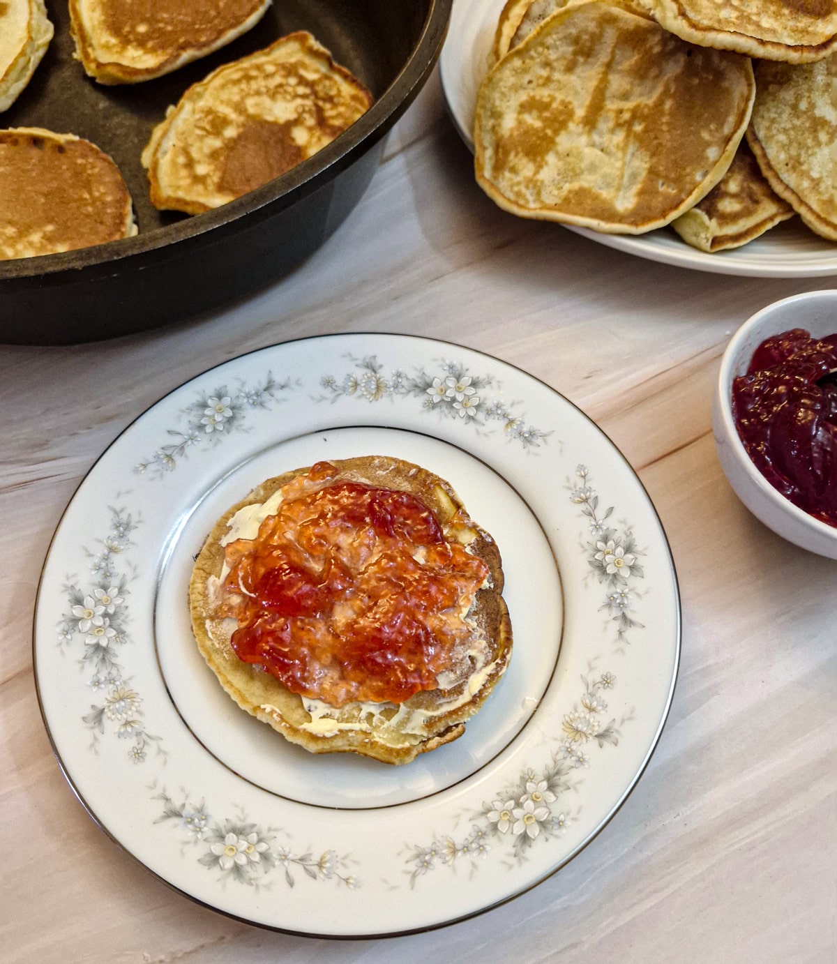 Close up of a drop scone which has been spread with butter and strawberry jam on a white plate.