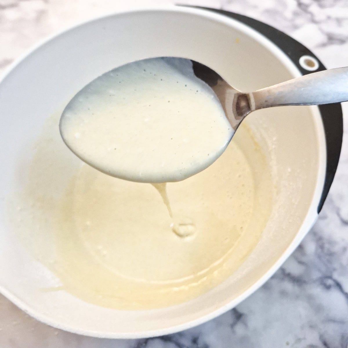 Drop scone batter being dripped from a large spoon into a mixing bowl to show the consistency.