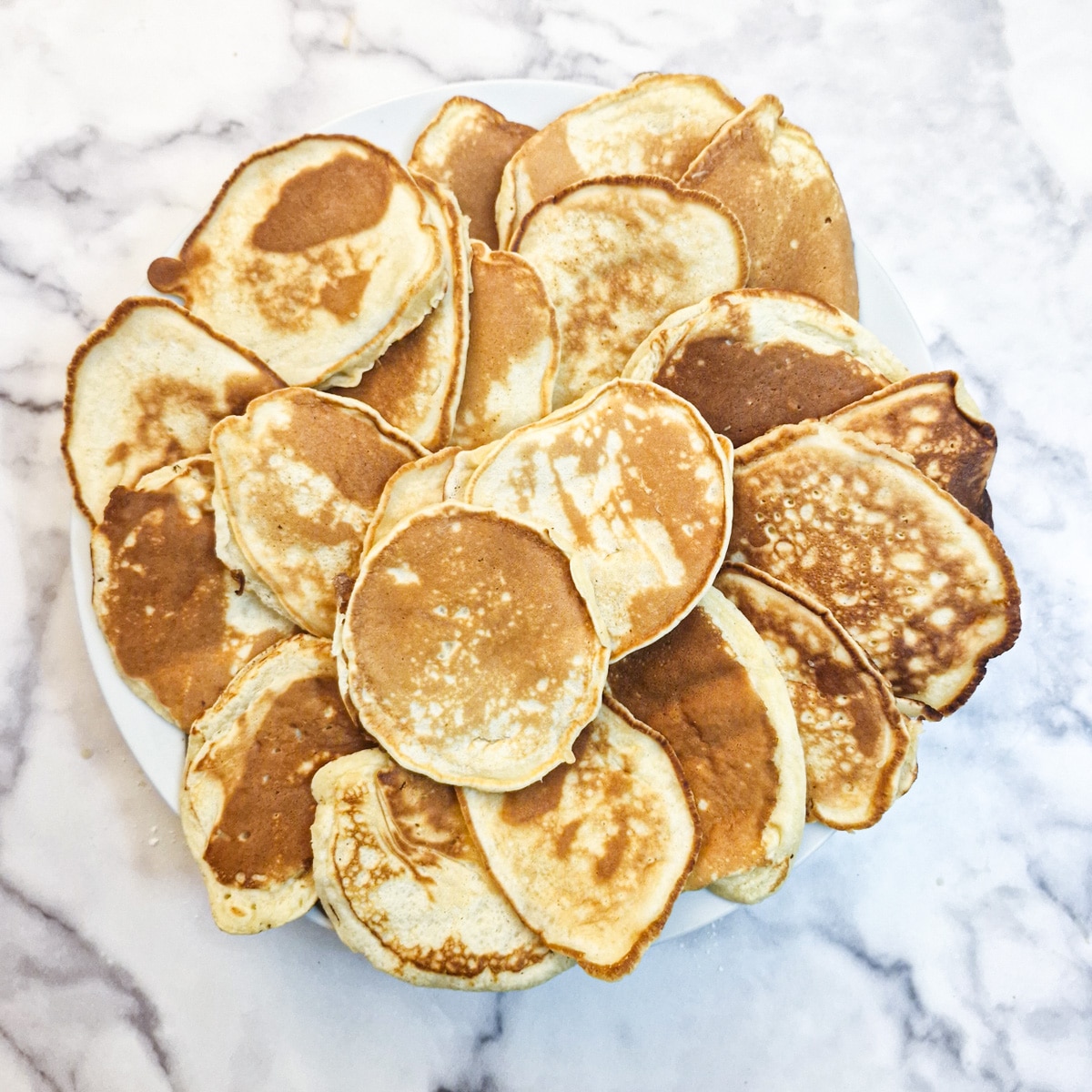 A pile of 24 drop scones arranged on a plate.