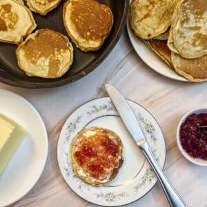 A drop scone spread with butter and jam on a white patterned plate.