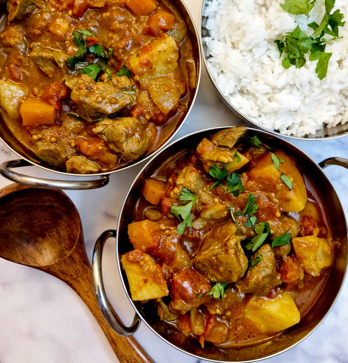 Two balti dishes containing lamb curry alongside a dish of white rice.