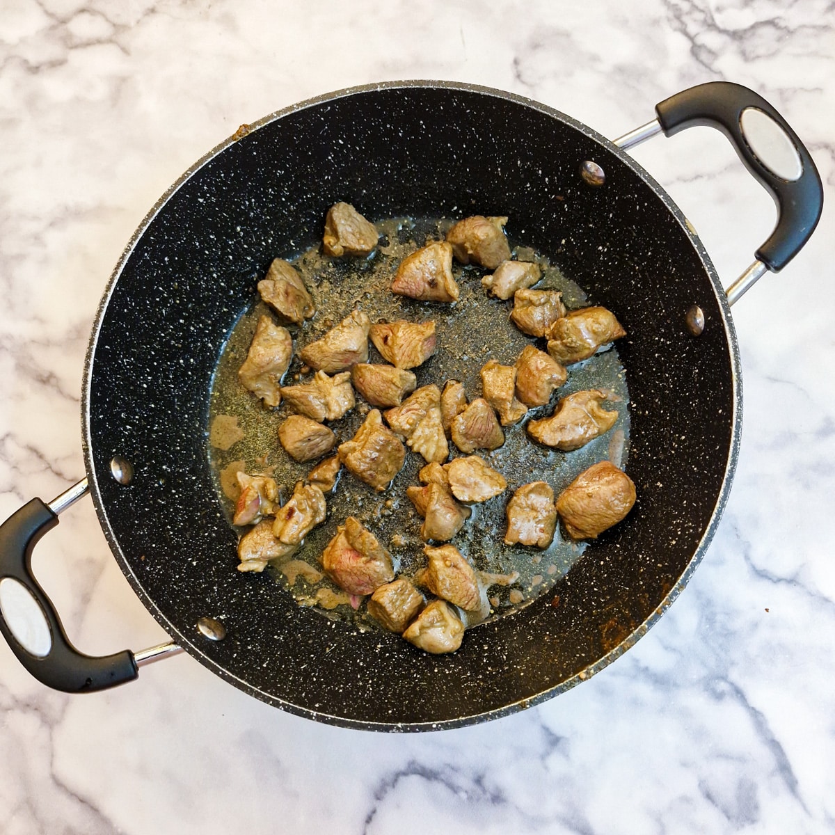 Cubes of lamb browning in a frying pan.