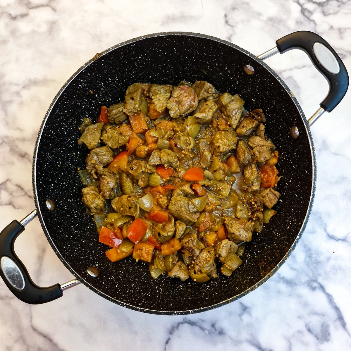 Lamb cubes and fresh tomatoes frying in a pan.