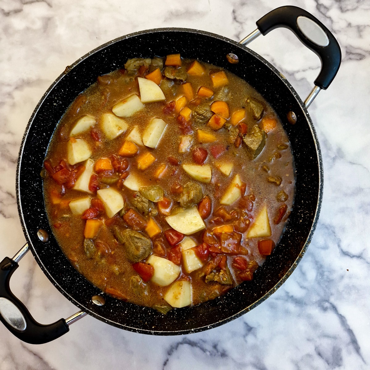 Stock, potatoes, carrots in a pan with cubed lamb, spices and onions.