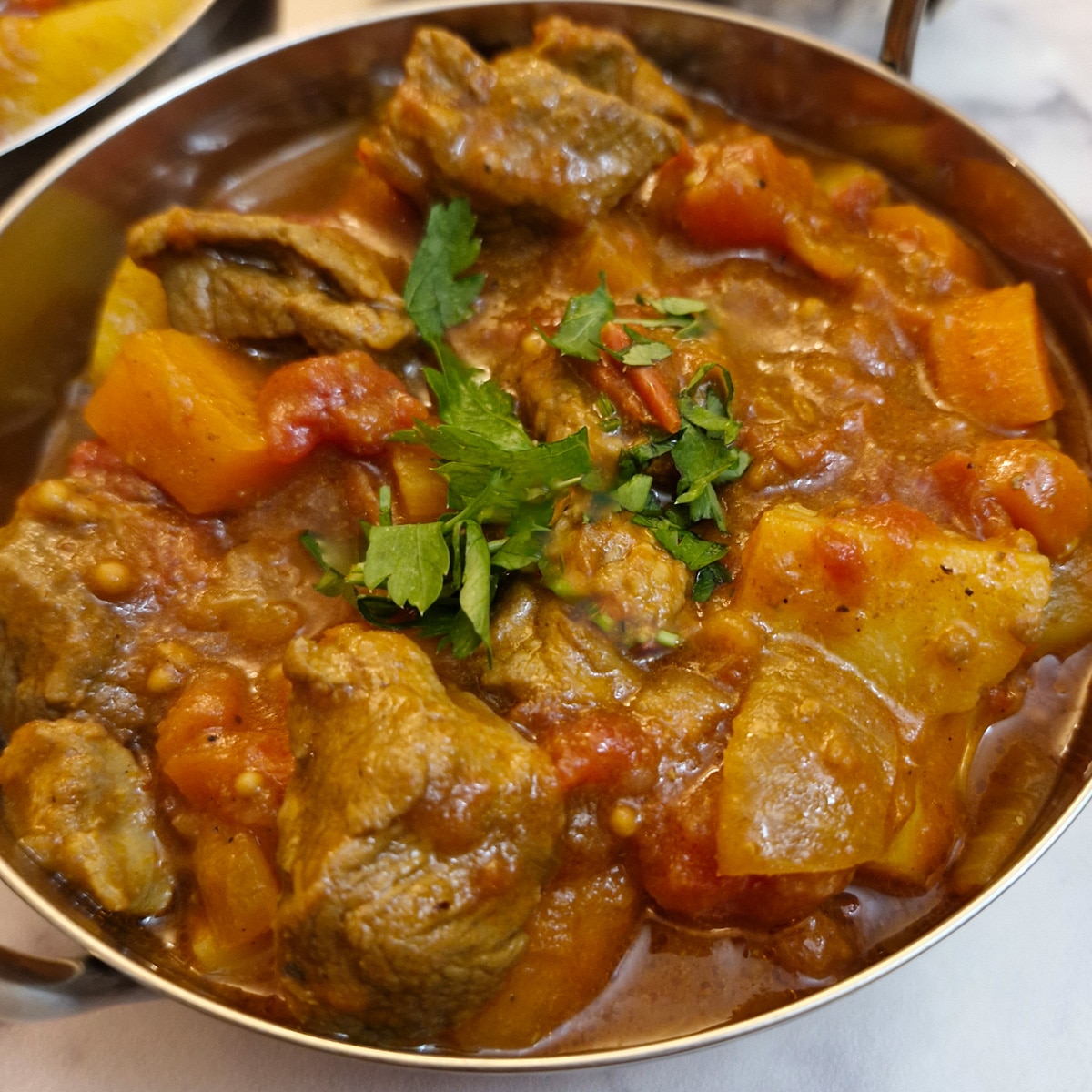 Lamb curry in a serving dish garnished with chopped coriander.