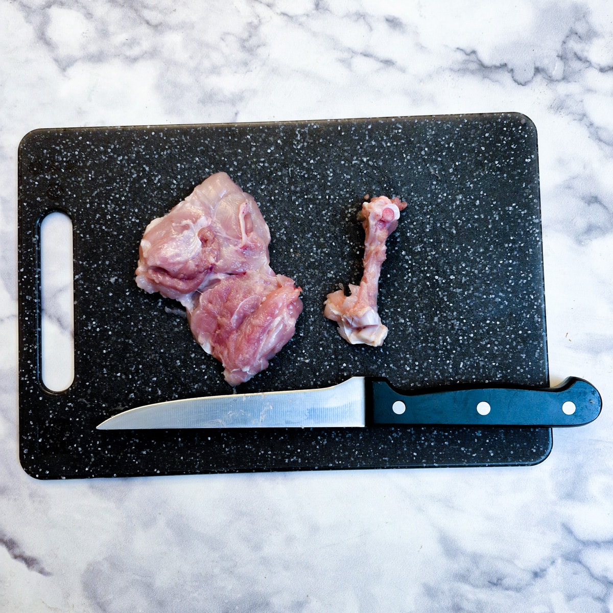 A deboned chicken thigh on a chopping board next to the bone that has been removed.