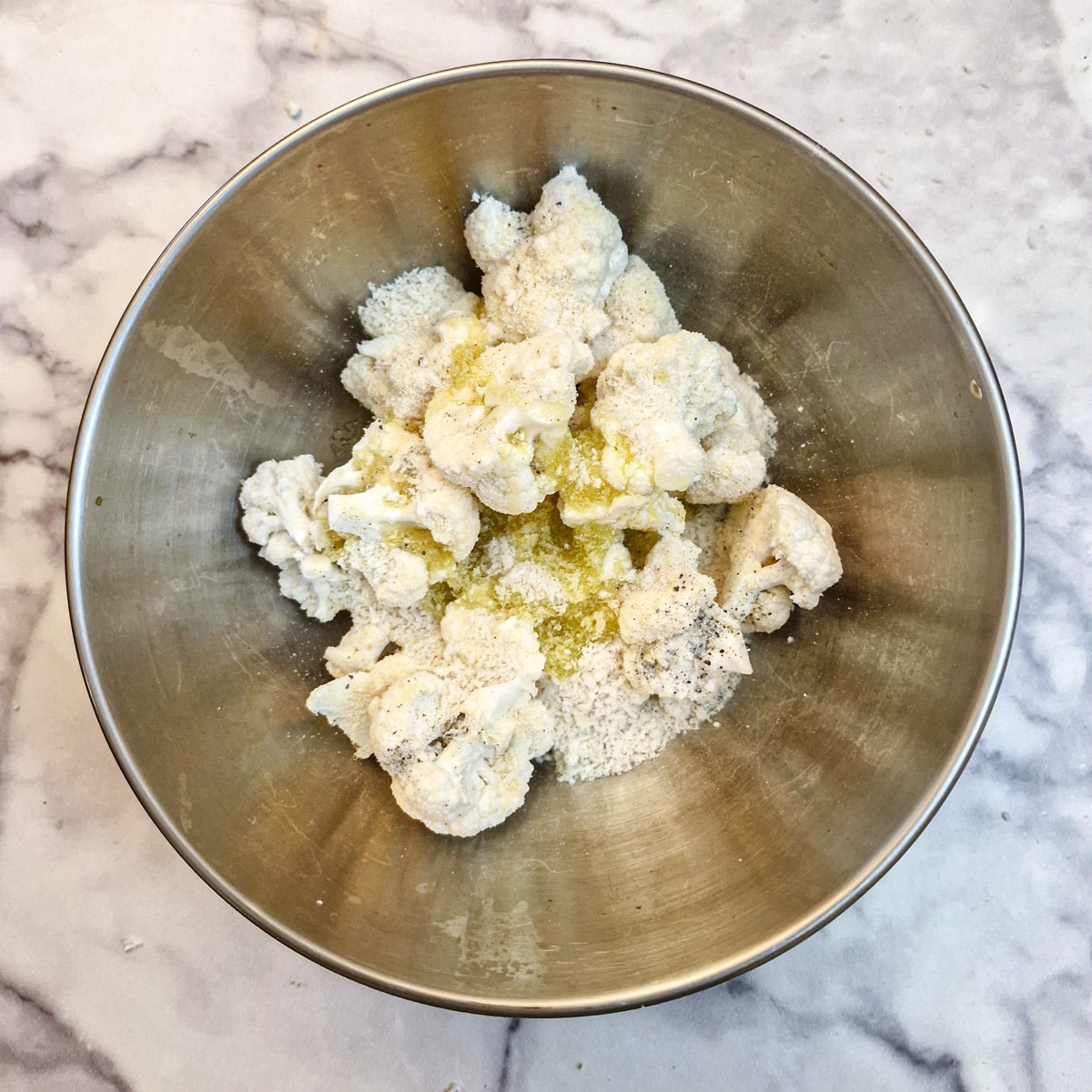 Cauliflower florets in a mixing bowl with olive oil, panko breadcrumbs and grated parmesan cheese.