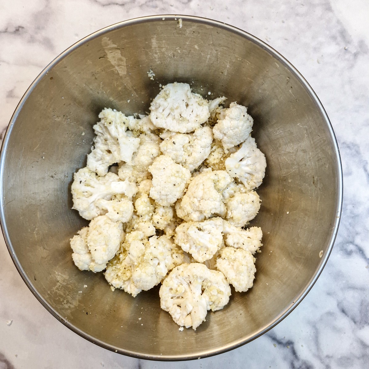 A stainless steel mixing bowl with cauliflower florets mixed the the other ingredients.